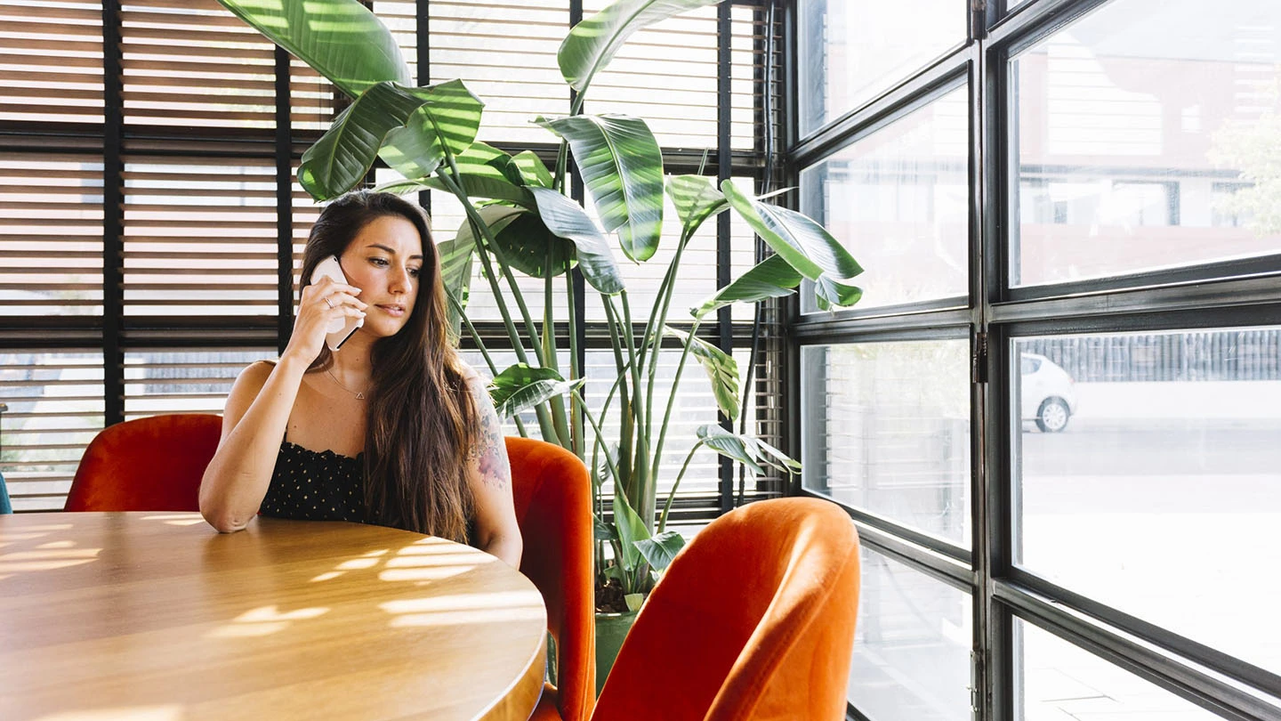 beautiful-young-woman-sitting-in-restaurant-talking-on-mobile-phone-scaled